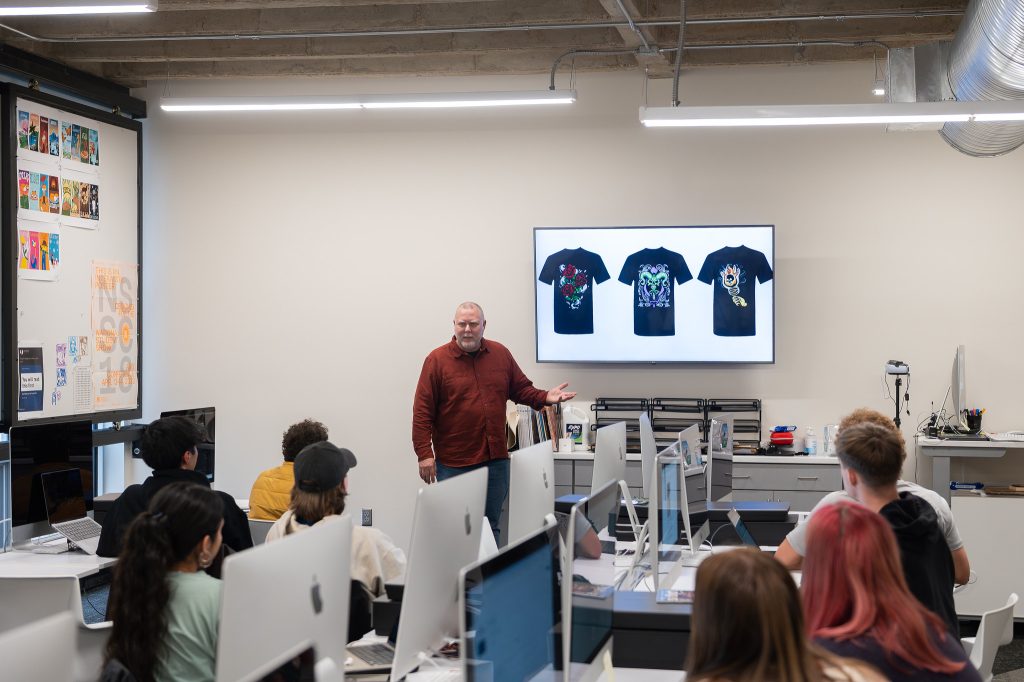 Jon Decker (professor) showing T-shirt examples on the screen to a class.